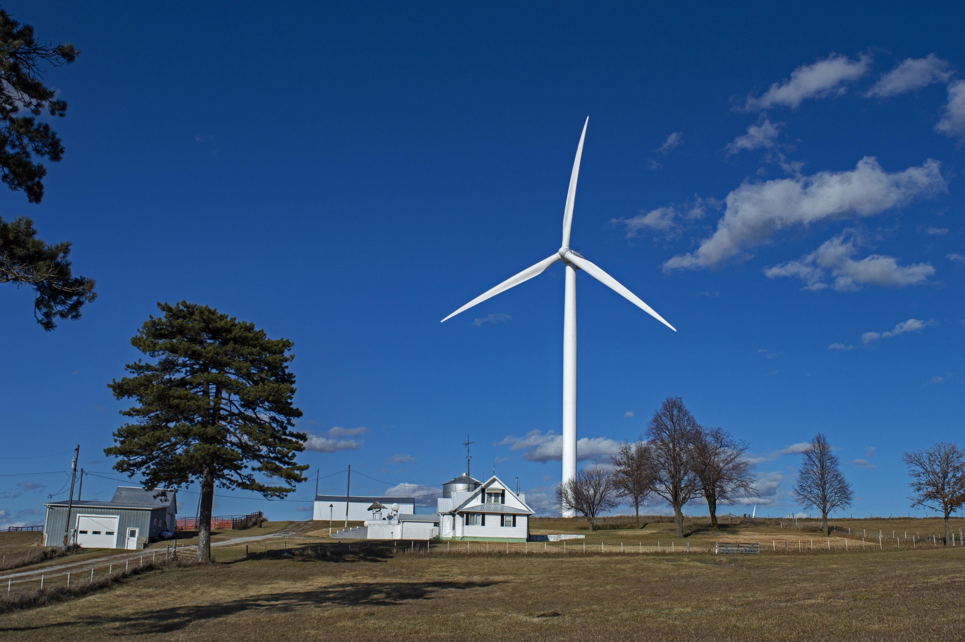 A large field with houses and a wind turbine at the back portraying one of the 7 simple ways to make your home sustainable.