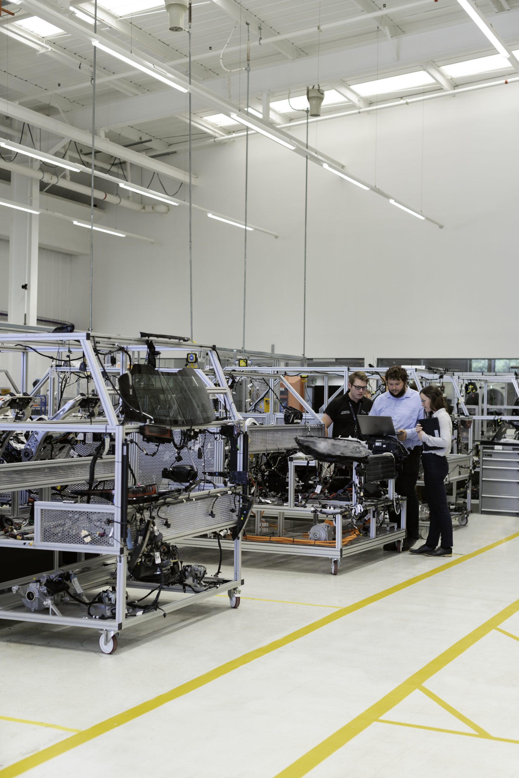 An engineering lab with machines and robotics and three engineers standing in a corner of the lab, going through content on a laptop. Portraying some insane engineering myths people still believe